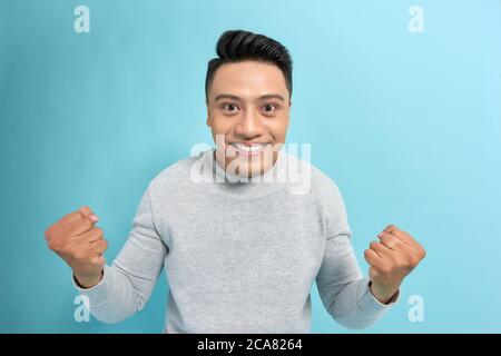 Jeune homme asiatique confiant dans des lunettes joyeusement montrant oui geste sur l'appareil photo sur fond bleu Banque D'Images