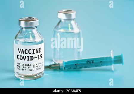 Flacon en verre avec étiquette Covid 19 vaccin (propre modèle, pas de produit réel), un autre flacon et une aiguille de seringue hypodermique à proximité, fond bleu clair Banque D'Images