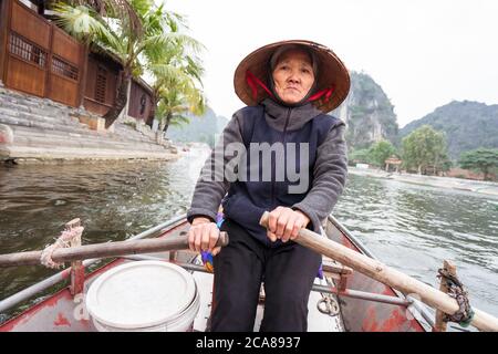 TAM COC / Vietnam - 25 janvier 2020: Vieille femme vietnamienne avec chapeau conique traditionnel bateau à ramer avec touristes dans le parc naturel Banque D'Images