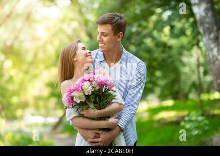 Célébration de l'anniversaire. Jeune fille avec des fleurs regardant affectueusement le petit ami dans le parc Banque D'Images