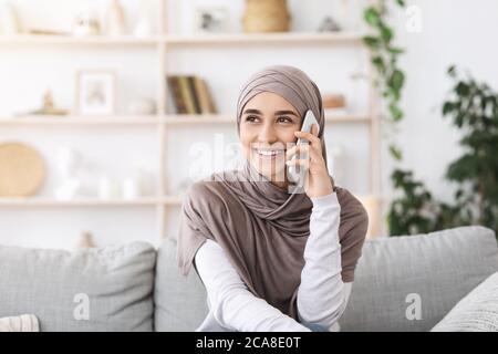 Appel attendu depuis longtemps. Bonne fille musulmane dans hijab avoir une conversation téléphonique à la maison Banque D'Images