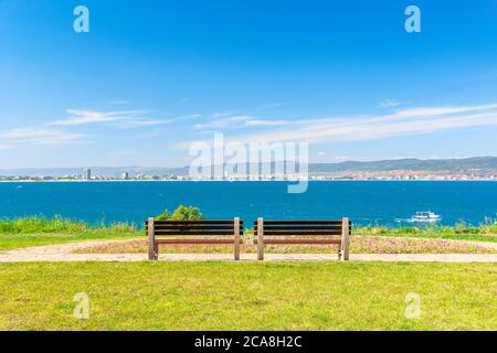 deux bancs sur la plage ensoleillée. belle vue depuis le sentier pavé sur la mer. ville et montagne au loin sous un ciel bleu avec le cloo Banque D'Images