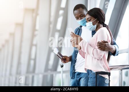 Couple noir de voyageurs portant des masques médicaux à l'aéroport, en attente de vol Banque D'Images