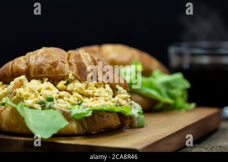 Gros plan sur des œufs brouillés farcis croissant sur un plateau en bois avec un fond de café chaud. Banque D'Images