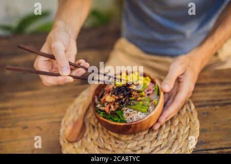 Homme mangeant bol de Poke avec crevettes, maïs, avocat, gingembre et champignons Banque D'Images