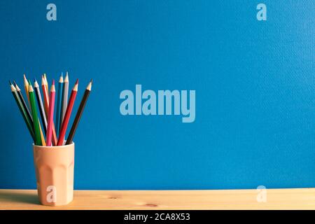 Crayons de couleur dans le support sur le bureau en bois avec fond bleu Banque D'Images