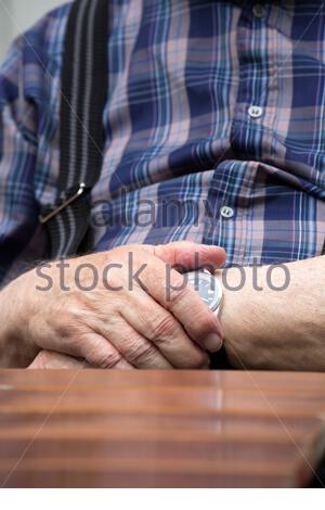 Les mains d'un vieil homme couvrent en partie sa montre alors qu'il est assis à une table en Allemagne Banque D'Images