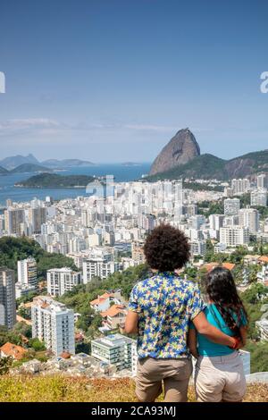 Un couple multiethnique bras dans bras avec vue sur la montagne du pain de sucre et les gratte-ciel de Rio, Rio de Janeiro, Brésil, Amérique du Sud Banque D'Images