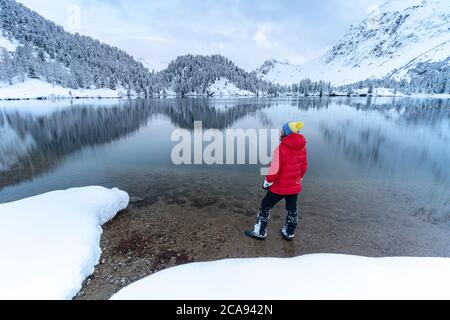 Homme debout sur les rives du lac Cavloc en admirant les forêts enneigées, vallée de Bregaglia, Engadine, canton de Graubunden, Suisse, Europe Banque D'Images