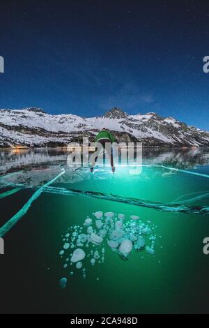 Homme patinant sur le lac gelé Sils illuminé de nuit par un chalumeau, Engadine, canton de Graubunden, Suisse, Europe Banque D'Images