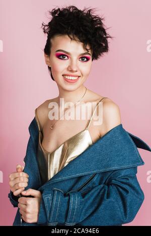 Une fille avec un grand sourire sincère est en studio sur un fond rose pastel. Une fille avec une étrange coiffure et maquillage lumineux volant Banque D'Images
