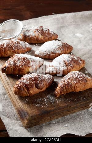 les croissants cuits saupoudrés de sucre en poudre se trouvent sur un panneau de bois marron, en gros plan Banque D'Images