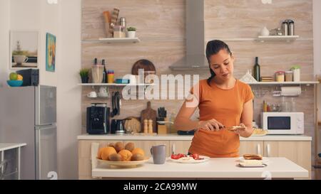 Femme qui répand du beurre sur du pain grillé pour le petit déjeuner. Couteau d'étalement de beurre doux sur une tranche de pain. Un style de vie sain, pour un délicieux repas du matin dans une cuisine confortable. Déjeuner traditionnel savoureux Banque D'Images