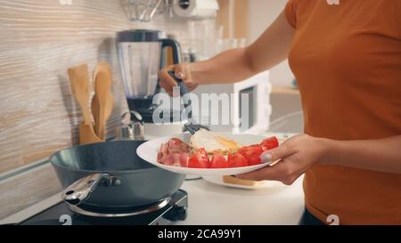 Femme de ménage cuisant des œufs pour le petit déjeuner dans la cuisine. Une matinée saine avec des produits frais, un mode de vie heureux pour la femme au foyer qui cuisine dans une cuisine moderne et confortable sous la lumière chaude et ensoleillée du matin d'été Banque D'Images