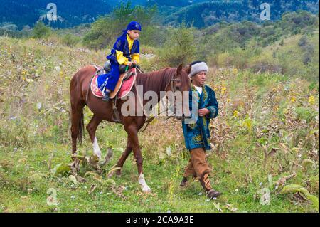 Balades autour de l'homme kazakh avec son fils sur un cheval après la cérémonie de circoncision Sundet Toi, Kazakh village ethnographique Aul Gunny, Talgar city, Al Banque D'Images