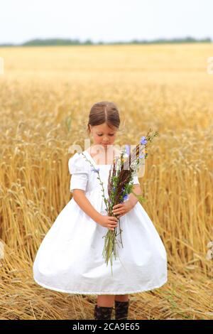 Petite fille avec un bouquet de fleurs sauvages dans ses mains dans un champ de blé. Banque D'Images