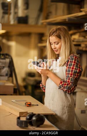 vue latérale sur une femme de bois de race blanche avec un smartphone, une femme chat avec un ami pendant qu'elle a du temps libre au travail Banque D'Images