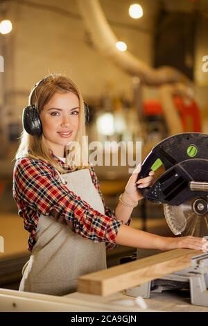 portrait de charpentier de dame attrayant à l'aide d'une scie circulaire, la femme fait des meubles en bois faits à la main sur une commande pour les clients. en atelier Banque D'Images