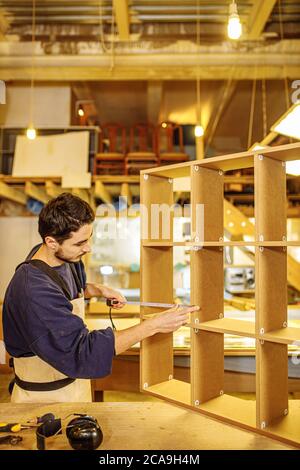 jeune menuisier construisant des étagères, meubles de maison. beau gars en uniforme pendant le travail à l'usine. vue latérale Banque D'Images