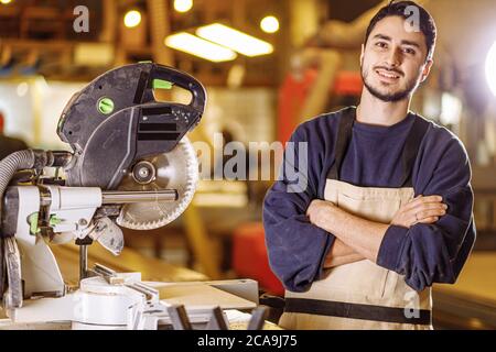 portrait du jeune caucasien menuisier positif sur le lieu de travail, beau gars dans les vêtements de travail sourire et regarder la caméra, aimez être menuisier Banque D'Images