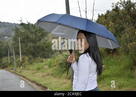 Latino brunette femme souriant en marchant dans une route avec un parapluie Banque D'Images