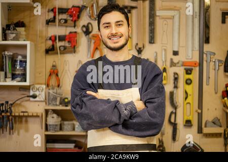 portrait du jeune caucasien menuisier positif sur le lieu de travail, beau gars dans les vêtements de travail sourire et regarder la caméra, aimez être menuisier Banque D'Images