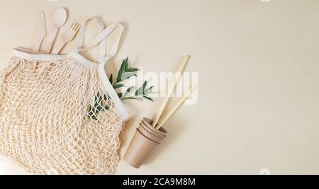 Sac en maille écologique avec couverts biodégradables, gobelets en papier, pailles en bambou et feuilles vertes. Concept de style de vie sans plastique et sans gaspillage. Vue de dessus, Banque D'Images