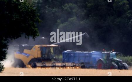 Une moissonneuse-batteuse vue par la brume thermique coupe une récolte d'orge de printemps dans un champ près d'Ashford, dans le Kent, alors que le temps chaud continue. Banque D'Images