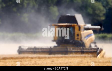 Une moissonneuse-batteuse vue par la brume thermique coupe une récolte d'orge de printemps dans un champ près d'Ashford, dans le Kent, alors que le temps chaud continue. Banque D'Images