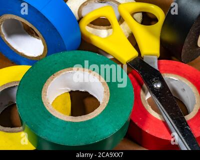 Gros plan POV de six rouleaux de ruban adhésif électrique / général domestique, dans une variété de couleurs, plus une paire de ciseaux. Banque D'Images