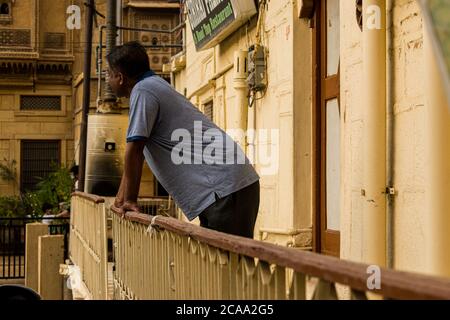 jaisalmer, rajasthan / inde - VERS juillet 2020 : l'homme d'âge moyen aime regarder à l'extérieur de sa maison, s'appuie sur la balustrade du balcon pendant la corona viru Banque D'Images