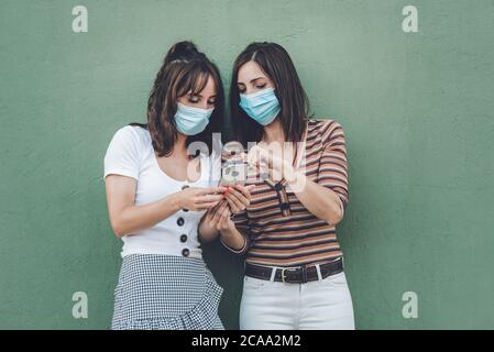 jeunes femmes amis portant un masque médical à l'aide d'un téléphone portable dans la rue Banque D'Images