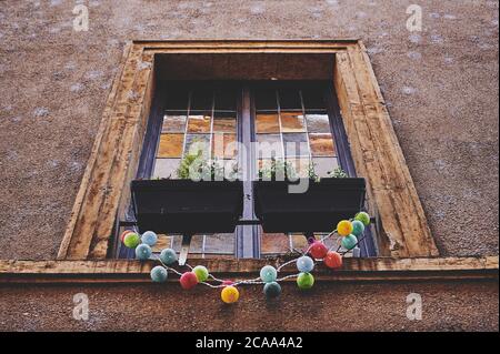 Vieille fenêtre française avec carreaux de verre de couleur et rebord de fenêtre en bois, chaîne lumineuse de couleur est accrochée à elle Banque D'Images