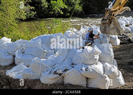 Une équipe de construction pour l'atténuation des crues utilisant une pelle hydraulique pour soulever de lourds sacs de roches afin de stabiliser les rives de la rivière Elbow, Calgary Canada Banque D'Images