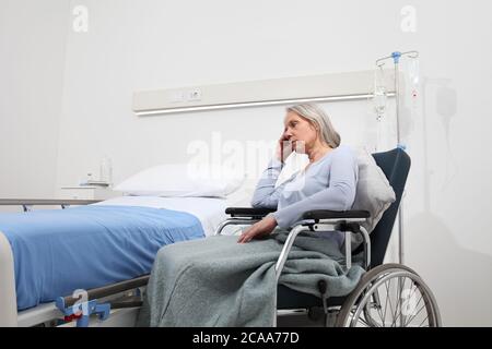 triste et pensive femme âgée abandonnée et oubliée isolée sur un fauteuil roulant près du lit dans la chambre d'hôpital, concept de solitude et de vieillesse Banque D'Images