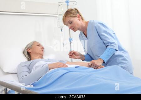 Femme âgée couchée dans le lit de la chambre d'hôpital, infirmière tenant l'aiguille pour relier l'IV au bras du patient Banque D'Images