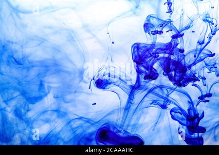 Encre bleue injectée dans l'eau à partir de la seringue, mélange de couleurs avec de l'eau créant des formes abstraites Banque D'Images