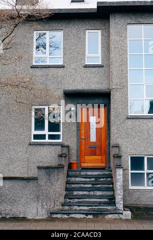 L'entrée est d'une porte en bois dans un bâtiment moderne de deux étages avec des fenêtres en plastique de différentes tailles et des marches avec des colonnes. Banque D'Images
