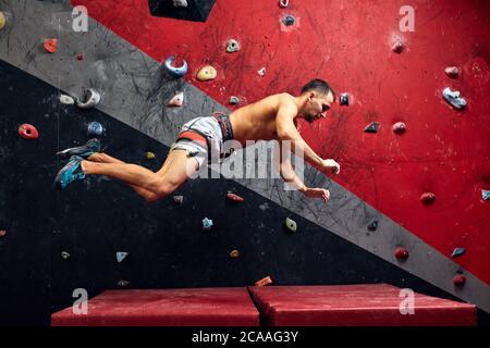 Photo de mouvement d'un grimpeur mâle tombant sur un tapis depuis le mur d'un grimpeur dans une salle d'escalade intérieure. Banque D'Images