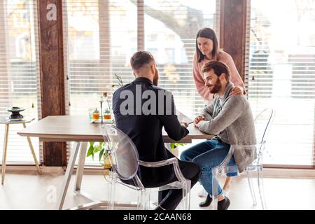 Avocat réussi donnant la consultation à un jeune couple familial attrayant environ dans son bureau moderne, l'achat de location d'appartement ou de maison. Banque D'Images