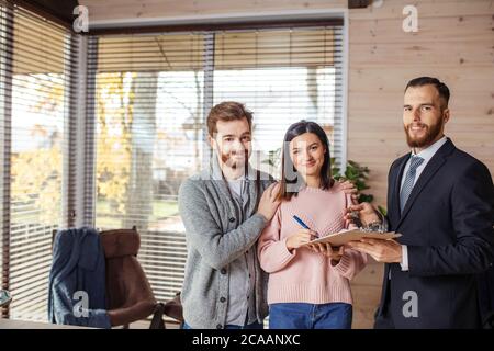 Smiling caucasian couple de locataires attrayant serrant la main de locateur, recevoir des clés de la chambre, faisant face a louer Banque D'Images