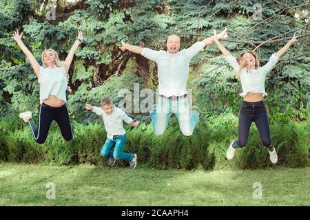 Des parents heureux avec une fille adolescente et un fils sautant tous ensemble au-dessus de l'herbe verte lumineuse dans le parc Banque D'Images