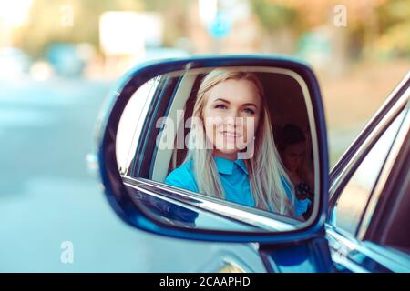 Réflexion dans le miroir de voiture latérale d'adulte belle femme en chemise bleue assis à l'intérieur et regardant l'appareil photo Banque D'Images