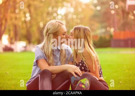 Femme et fille de l'adolescence donnant baiser les uns aux autres tout en se câlinant sur la pelouse verte d'été dans le parc Banque D'Images