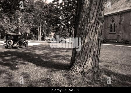 Vue sur une vieille rue de Stratford, Ontario. Une vieille voiture, le tronc d'un grand arbre, les maisons, la végétation et le mur de la cathédrale. Août 2020. Banque D'Images