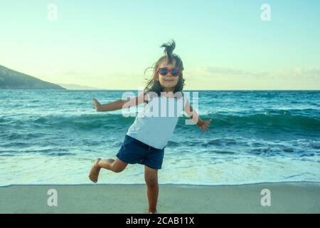 Petite fille qui étire ses bras à la plage en regardant l'appareil photo