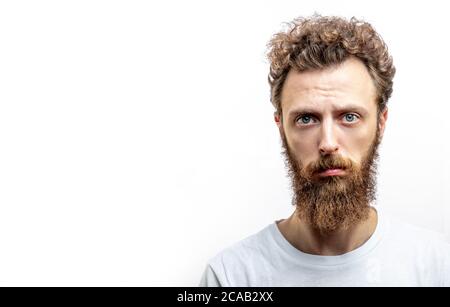 Photo en studio d'un homme européen triste et séduisant avec moustache et barbe, offensé et contrarié, debout sur fond blanc. Banque D'Images