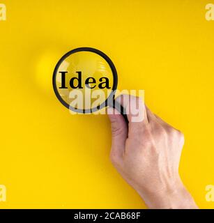 Vue en hauteur d'une main tenant une loupe Texte [idée] sur fond jaune Banque D'Images
