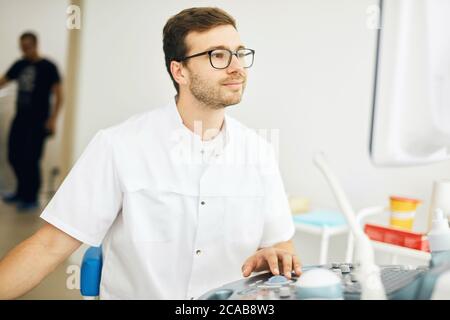 souriant médecin gentil regardant l'ordinateur et utilisant l'échographe. le thérapeute remarque une nouvelle vie dans le ventre d'une femme Banque D'Images