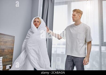 une jeune fille offensée caucasienne se tient dans une couverture une maison, son petit ami essayer de parler avec elle, s'excuse. à la maison Banque D'Images